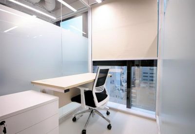 Private glass-walled office with a white desk and ergonomic chair.