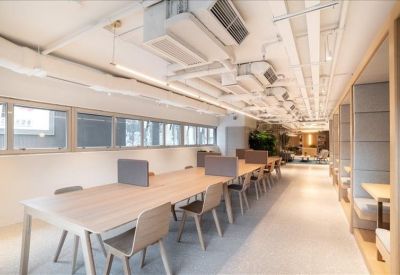 Long communal wooden work table in a bright, modern corridor space.