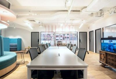 Open-plan workspace with a long white desk, black mesh chairs, and teal accents.