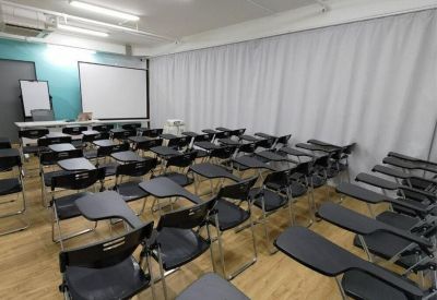 Classroom-style meeting room with rows of black tablet chairs and a projection screen.