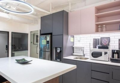 Modern communal kitchen with grey cabinetry, pink shelving, and a large white island.