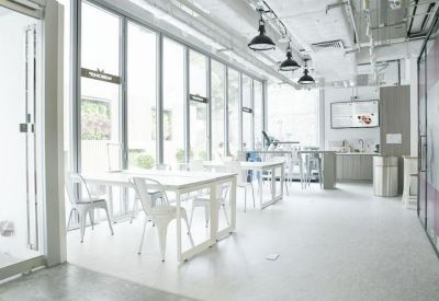 Sunlit coworking space with white tables, chairs, and floor-to-ceiling windows.
