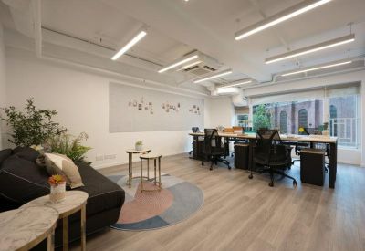 Open-plan workspace with a long wooden desk, black ergonomic chairs, and a dark sofa.