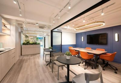 Spacious communal lounge and meeting area with orange armchairs, blue feature wall, and wood flooring.