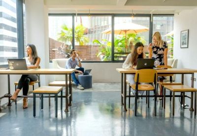 Open-plan coworking space with long wooden tables and large windows.