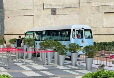 Public shuttle bus waiting at a designated pickup point with silver planters.
