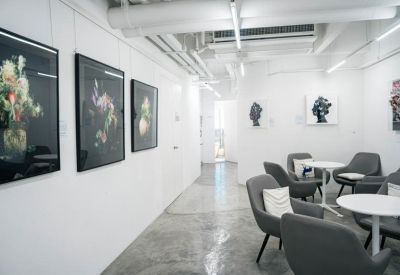 Bright communal lounge featuring modern grey armchairs and floral art on white walls.