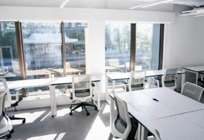 Bright coworking area with rows of white desks and views through floor-to-ceiling windows.