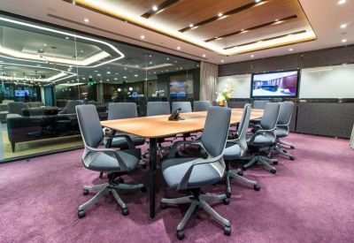 Large boardroom with a long wooden table, gray chairs, and a wall-mounted screen.