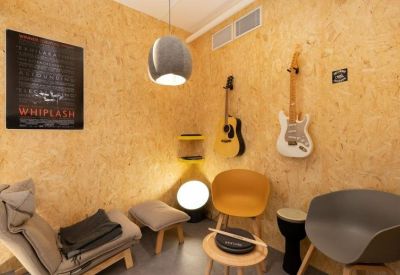 Vibrant breakout room with OSB wood walls, hanging guitars, and comfortable lounge seating.