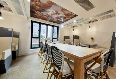 Long communal wooden table under a decorative ceiling mural and warm pendant lighting.