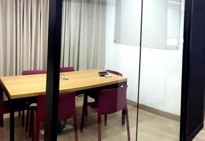 Meeting room with a long wooden table, maroon chairs, and glass walls.