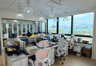 Bright office space with multiple workstations, light wood flooring, and large windows overlooking the water.