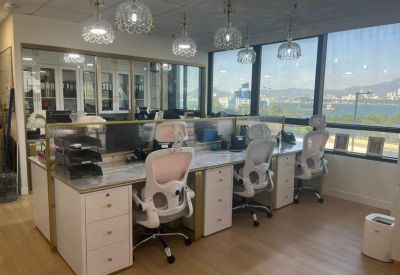 Open-plan workspace featuring white desks, ergonomic chairs, and modern pendant lighting by a large window.