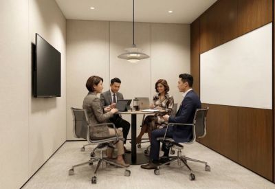 Four people in a professional meeting room with a round table, wall-mounted screen, and wood paneling.