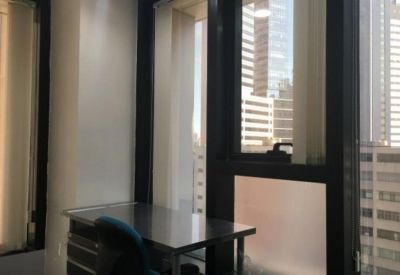 Private office workstation with a metal desk situated by a large window overlooking city buildings.