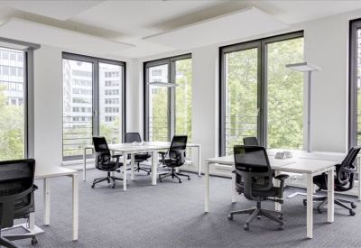 Bright open-plan office with white desks and black mesh chairs by large windows.