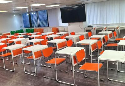 Spacious classroom setup with rows of white desks and vibrant orange chairs.