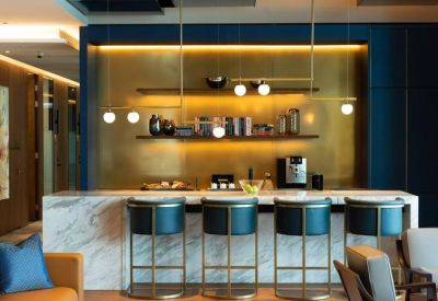 Lounge area with a marble bar counter, teal stools, and a gold feature wall.