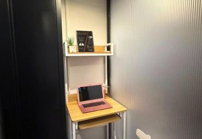 Compact private office booth with a wooden desk, white chair, and glass partition.