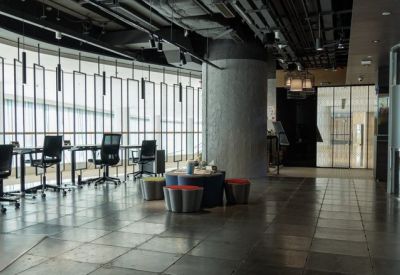 Spacious coworking lounge with circular stools, a large concrete pillar, and views of the harbor.