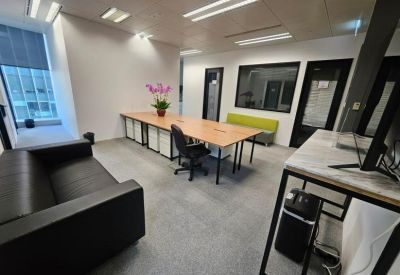 Spacious office lounge area with a leather sofa, long work table, and purple orchid plant.