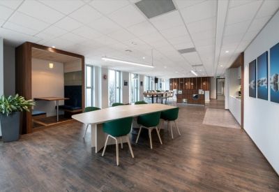 Modern communal area with a long wooden table, green velvet chairs, and a private wooden booth.