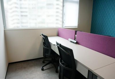 Shared workspace featuring white desks and purple privacy dividers near a large window.