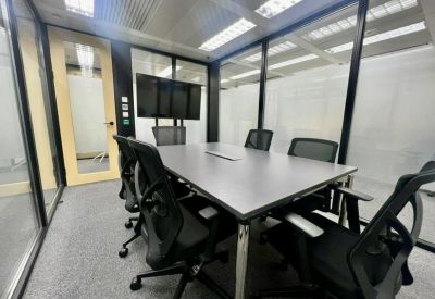 Modern glass-walled meeting room with a grey table and black ergonomic chairs.