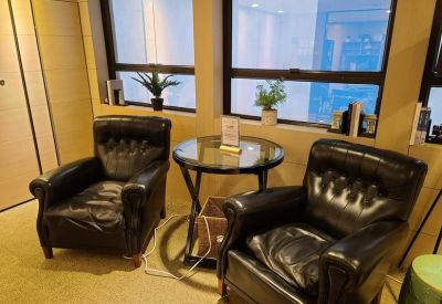 A cozy lounge area with two black leather armchairs and a glass side table by a window.