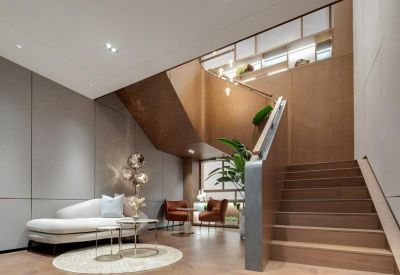 A warm lounge area featuring a curved white sofa, wooden stairs, and a contemporary light fixture.