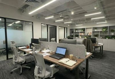 Bright open-plan office with wooden desks, ergonomic chairs, and modern overhead lighting.