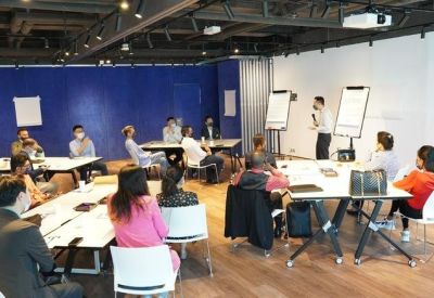 Professional meeting room with a presentation in progress and rows of white desks.