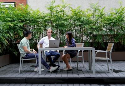 Three people having a meeting at a table on an outdoor deck surrounded by lush greenery.