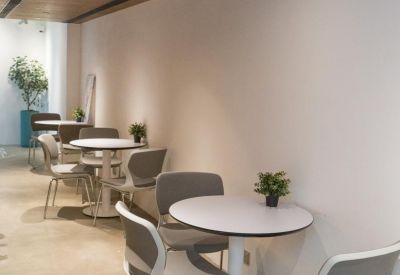 Bright, modern corridor featuring small round tables, grey chairs, and a light wood ceiling.