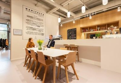 Collaborative office workspace with a long white table, wooden chairs, and a café-style bar.