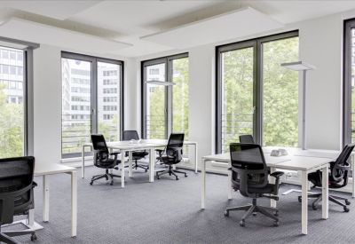 Open office area featuring multiple workstations and large windows with leafy views.
