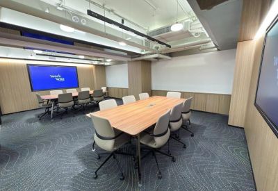 Spacious boardroom with a large wooden table, grey chairs, and a digital presentation screen.