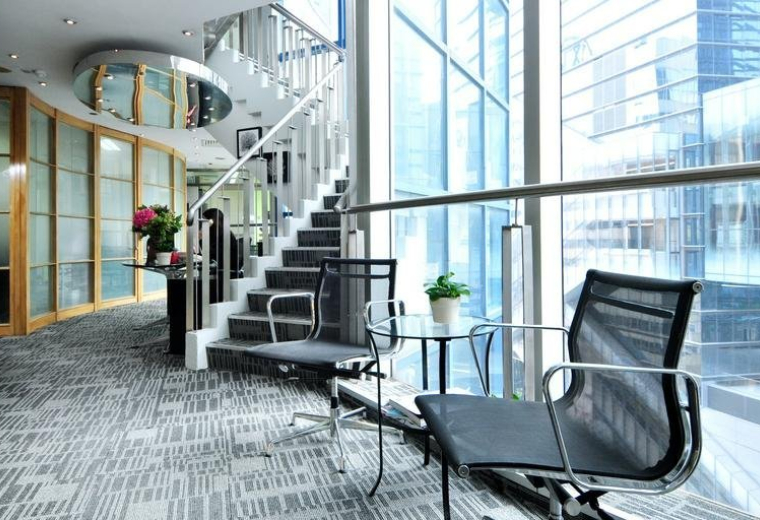 Modern lounge area with mesh chairs, glass table, and a spiral staircase.