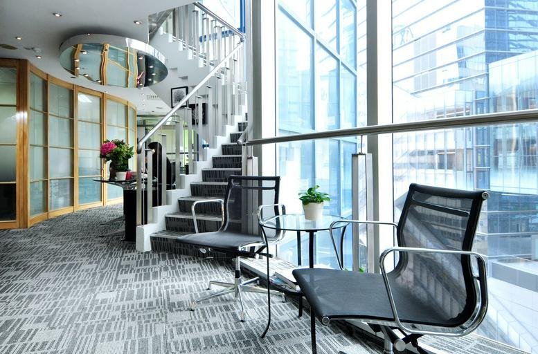 Modern lounge area with mesh chairs, glass table, and a spiral staircase.