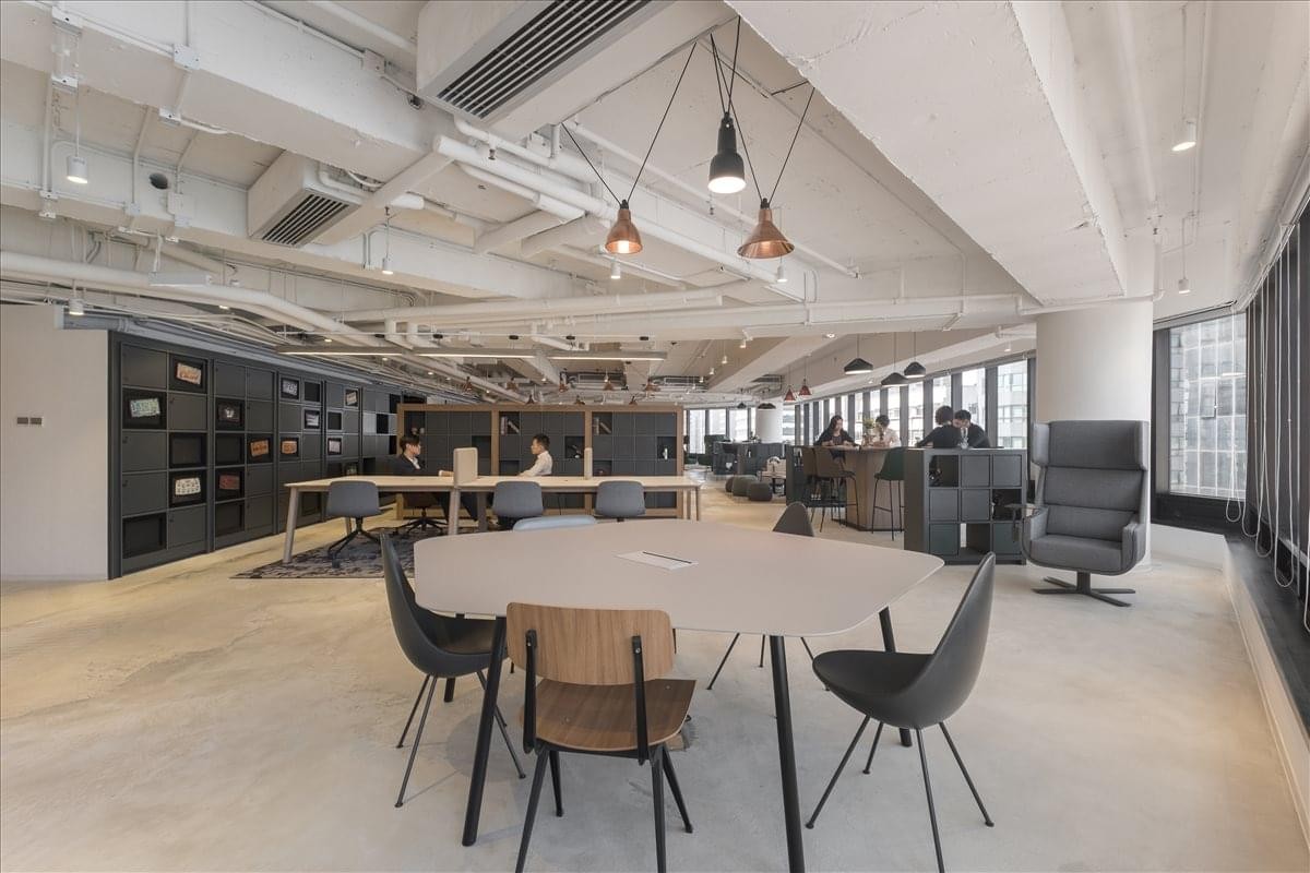 Spacious coworking area with a round feature table and exposed ceiling pipes.