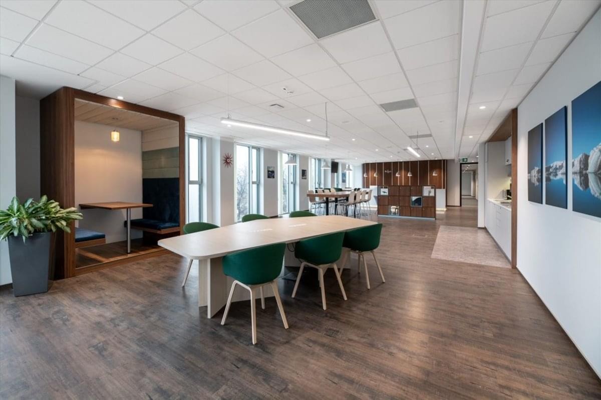 Bright communal dining area featuring a long wooden table and green velvet chairs.