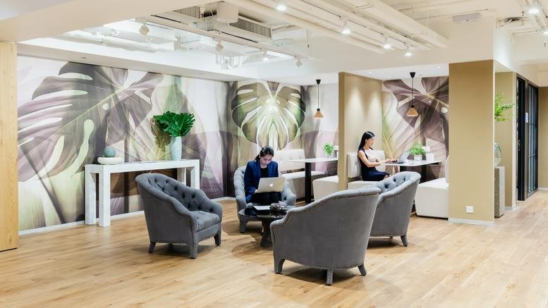 Spacious lounge at Nexxus Building with tropical wallpaper, grey armchairs, and warm wooden flooring.