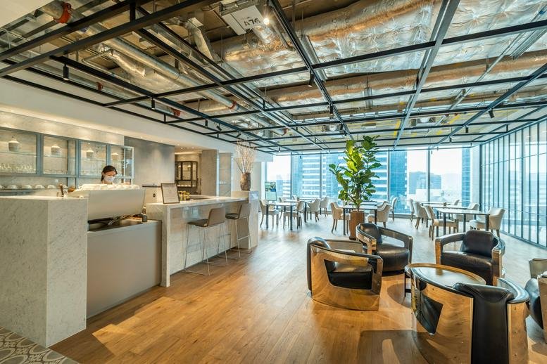 Spacious communal lounge and cafe area with warm wood floors and industrial ceiling at One Island East.