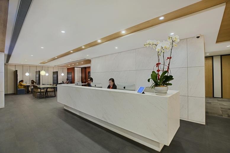 Bright reception area at The Hong Kong Club Building with a sleek white desk and floral arrangement.