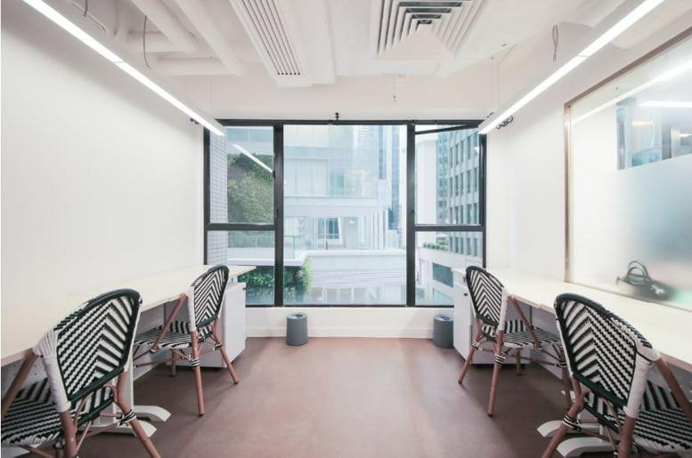 Bright shared workspace at World Trust Tower featuring minimalist desks and large city-view windows.