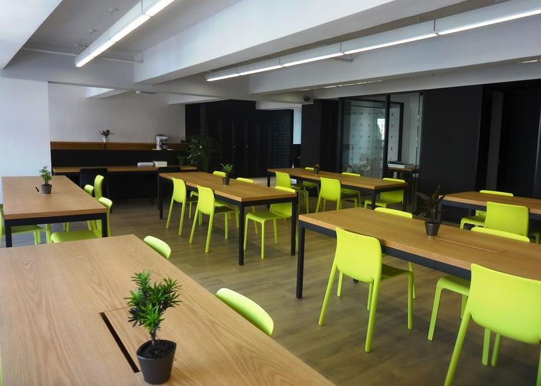 Spacious communal coworking area featuring wooden tables and vibrant lime green chairs.