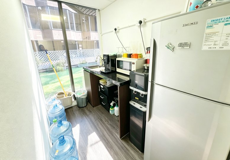 Compact office pantry with a coffee machine, microwave, and water dispenser near a large window.