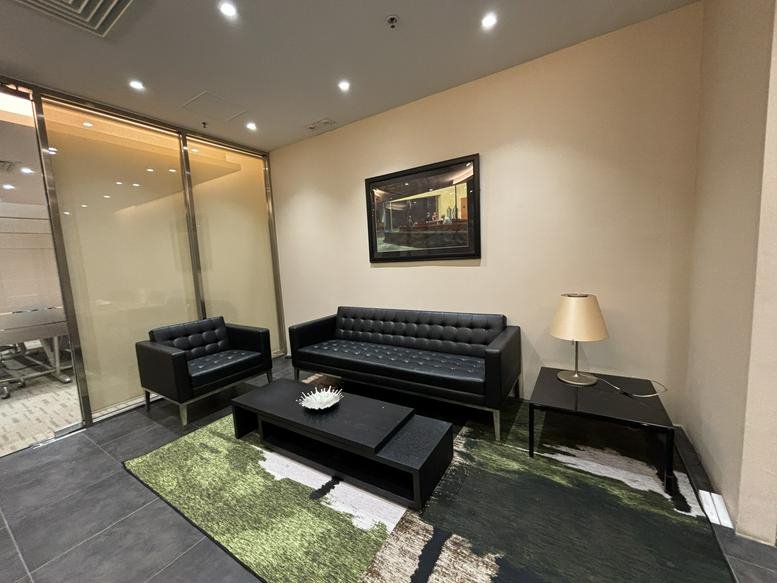 Reception waiting area with black leather tufted sofas and a green patterned rug.