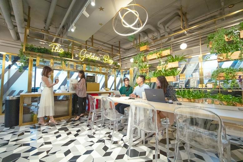 Vibrant communal lounge with patterned flooring, indoor plants, and a cafe-style seating area.